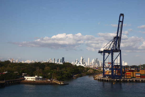 Puerto de carga con grúa y contenedores de envío a lo largo de la entrada al Canal de Panamá, con la ciudad de Panamá en el fondo
. - Foto, Imagen