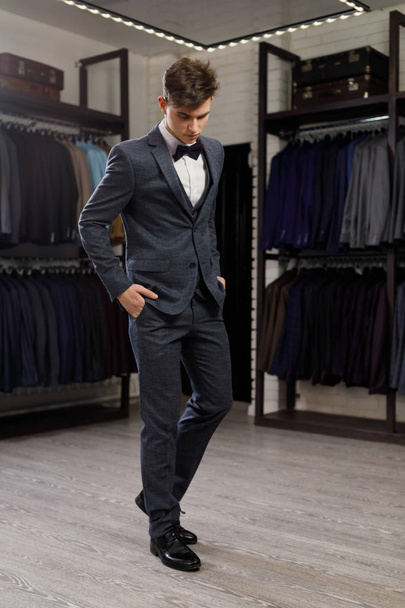 young man in classic vest against row of suits in shop - Foto, afbeelding