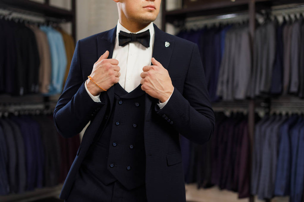 client is elegant guy trying on a suit in a mirror shop. In the background classic suits and jackets - Foto, immagini