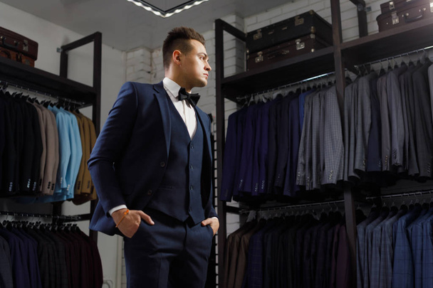 client is elegant guy trying on a suit in a mirror shop. In the background classic suits and jackets - Foto, afbeelding