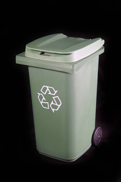 Grüner Recycling-Müll oder Mülleimer mit dem Recycling-Symbol auf schwarzem Hintergrund. - Foto, Bild