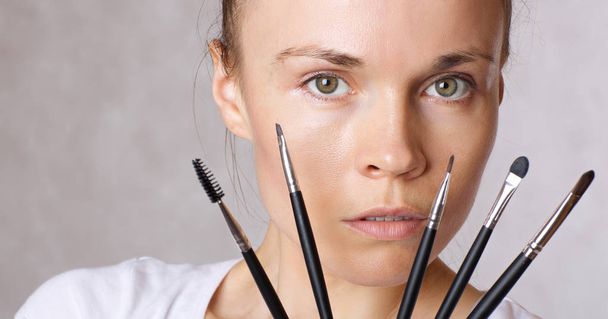 Jeune femme caucasienne garde kit pinceaux de maquillage près de son visage. Gros plan
 - Photo, image