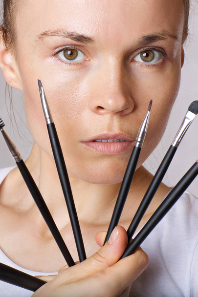 Young caucasian lady is keeping make up brushes kit close to her face. Closeup - Photo, Image