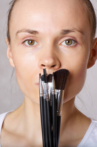 junge kaukasische Dame hält Make-up-Bürsten dicht vor ihrem Gesicht. Nahaufnahme - Foto, Bild