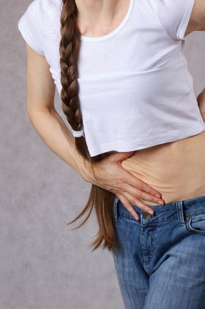 Young lady between 30 and 40 years old dressed in jeans has a pain in the belly. Closeup - Photo, Image