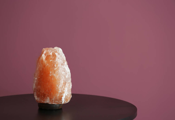 Himalayan salt lamp on table against color background - Foto, afbeelding