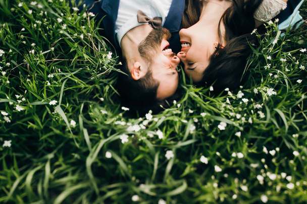 Overhead view of young couple smiling and laying on field with wildflowers - Fotó, kép