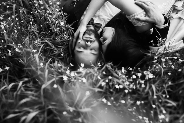 Overhead view of young couple smiling and laying on field with wildflowers - Фото, изображение