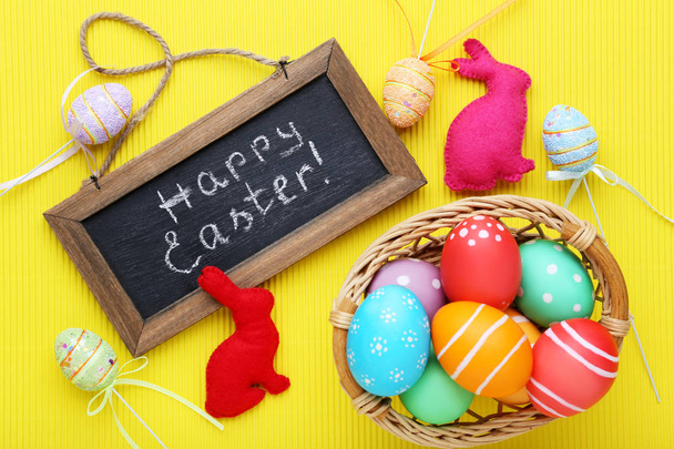 Inschrift Frohe Ostern auf Holzrahmen mit bemalten Eiern und Stoffhasen - Foto, Bild