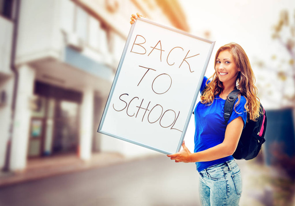 Щаслива дівчина-підліток зі шкільною сумкою тримає знак Назад до школи
  - Фото, зображення