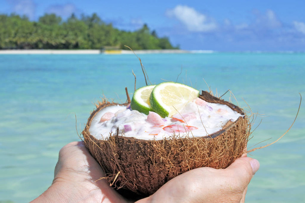 Mujer sostiene plato de ceviche servido en una cáscara de coco contra una isla
 - Foto, Imagen