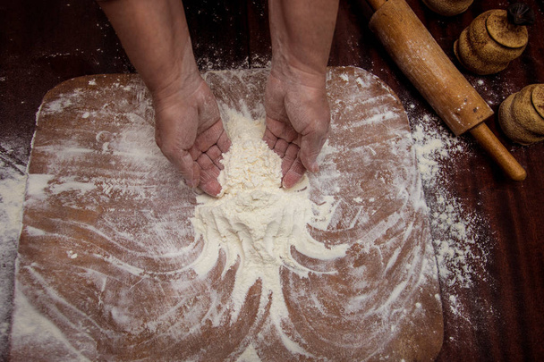 Μια γυναίκα μαγείρισσα πασπαλίσετε αλεύρι πάνω ένα ξύλο κοπής. Το μαγείρεμα. Κάνει το ψωμί στο τραπέζι της κουζίνας. Μαγειρική διαδικασία έννοια - Φωτογραφία, εικόνα
