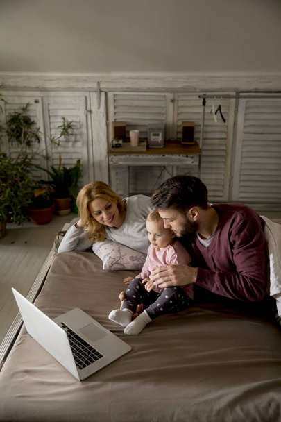 Happy family lies on bed and watching something on laptop in the bedroom - Photo, Image