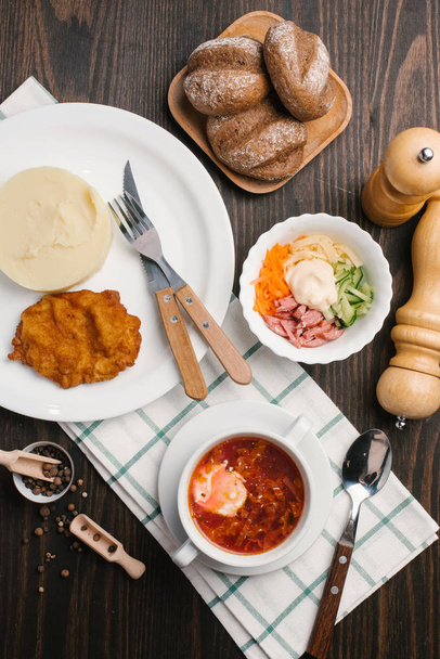 Top view of soup, mashed potato with schnitzel, salad and bread served on wooden table - Photo, Image