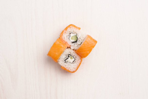 Top view of maki sushi with salmon, Philadelphia cheese and cucumber served on beige wooden surface - Φωτογραφία, εικόνα