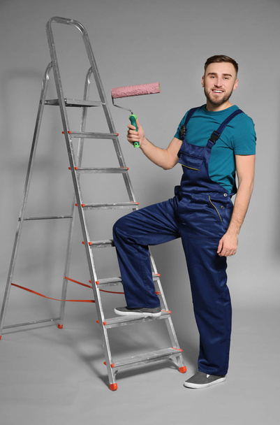 Young male decorator with paint roller on color background - Fotoğraf, Görsel