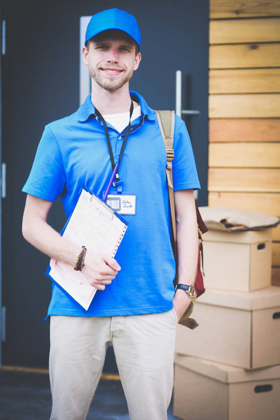 Lächelnder Zusteller in blauer Uniform bringt Paketkasten zum Empfänger - Kurierdienst-Konzept - Foto, Bild