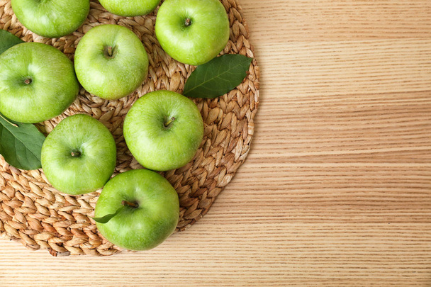 Wicker mat with fresh green apples on wooden background, top view - Foto, afbeelding
