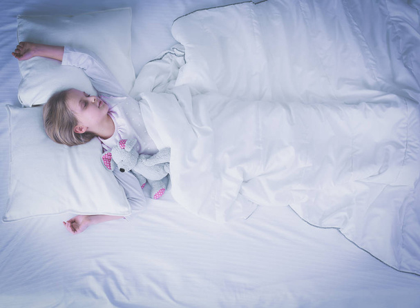 Child little girl sleeps in the bed with a toy teddy bear - Foto, Imagen