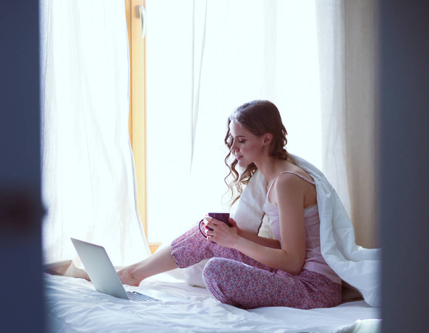 Young beautiful woman sitting in bed with laptop - Valokuva, kuva
