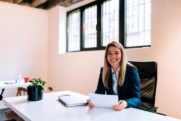Successful business concept. Smiling blonde business woman sitting at the bright office. Looking at camera. - Photo, Image