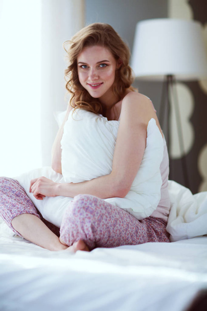 Young woman holding a pillow while sitting on her bed - Foto, Bild