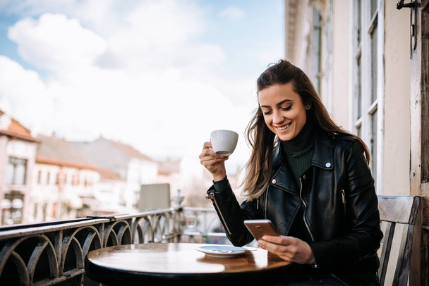 Girl enjoying cup of coffee while using phone on the balcony. - Zdjęcie, obraz