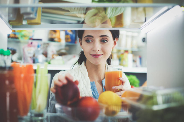 Sağlıklı yiyecek, sebze ve meyvelerle dolu açık buzdolabının yanında duran kadın portresi. - Fotoğraf, Görsel