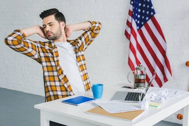 Freelancer cansado estirándose por mesa de trabajo en oficina ligera
 - Foto, imagen