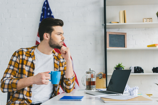 Nachdenklicher Mann trinkt Kaffee am Arbeitstisch im Home Office - Foto, Bild