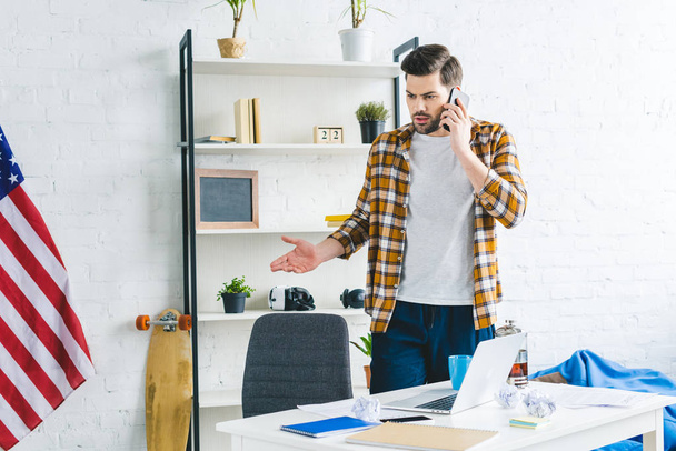 Freelancer seisoo pöydän ääressä ja puhuu puhelimessa kevyessä toimistossa
 - Valokuva, kuva