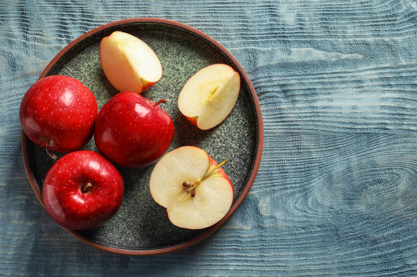 Тарілка зі свіжими стиглими червоними яблуками на дерев'яному фоні, вид зверху
 - Фото, зображення