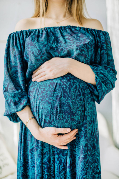 Pregnant woman in blue dress holding her stomach. - Fotografie, Obrázek