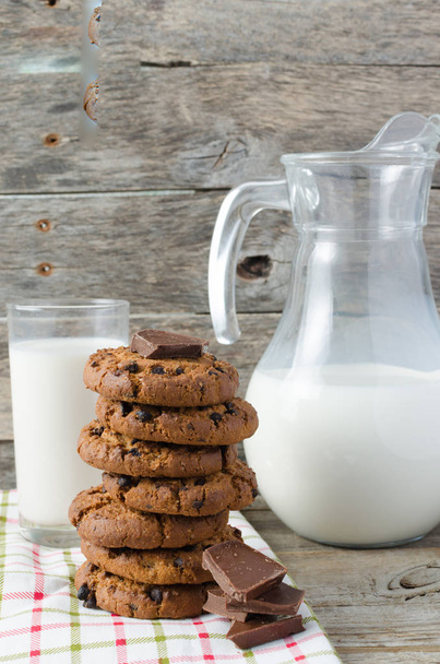 Oatmeal chocolate chip cookies, jug and glass of milk, rustic wooden background. - Foto, immagini