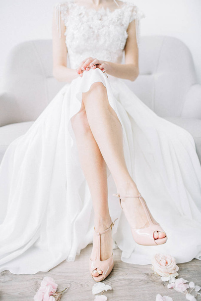 Fiatal menyasszony meztelen lábak rózsaszín magas sarkú cipő és a rózsaszín virágszirmok kanapén ül. Ünnepi esküvői divat fogalma. - Fotó, kép