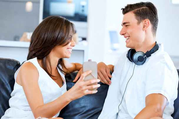 Young couple looking at mobile phone while sitting at home - Foto, immagini