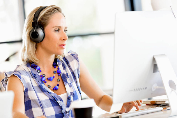 Young woman in the office with headphones - Foto, afbeelding