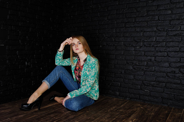 Stylish blonde girl in jacket and jeans against brick black wall - Foto, Bild