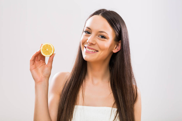 Beautiful brunette woman holding slice of lemon. - Фото, изображение