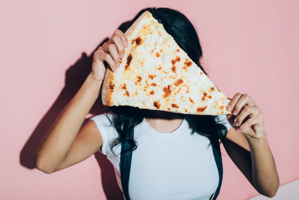obscured view of woman covering face with piece of pizza on pink background - Fotografie, Obrázek