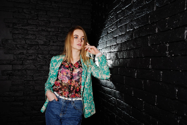 Stylish blonde girl in jacket and jeans against brick black wall - Valokuva, kuva