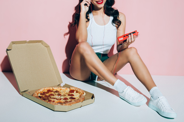 bijgesneden schot van lachende vrouw met retro speler en levering muziekdoos met pizza op roze achtergrond - Foto, afbeelding