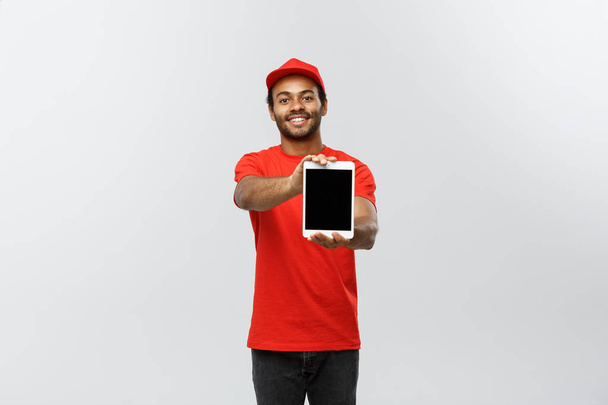 Delivery Concept - Portrait of Handsome African American delivery man or courier showing tablet on you to check the order. Isolated on Grey studio Background. Copy Space. - Fotoğraf, Görsel
