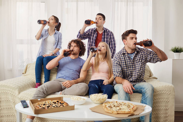 A group of friends are drinking beer from a bottle in the room. - Fotoğraf, Görsel