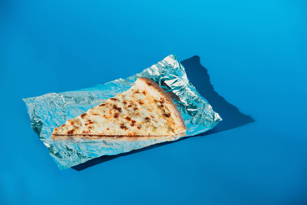 primer plano vista de pedazo de queso pizza italiana sobre papel de aluminio sobre fondo azul
 - Foto, Imagen