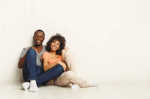 Афро-американская пара обнимается, сидит на полу
 - Фото, изображение