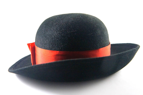 Zwarte hoed, muts, lady hoed, voelde hoed, ronde hoed met hoed met lint met rood lint, rode boog, zendspoel, rode, witte achtergrond, close-up, accessoires, kleding, mode, stijl. Kop stock beeld. - Foto, afbeelding