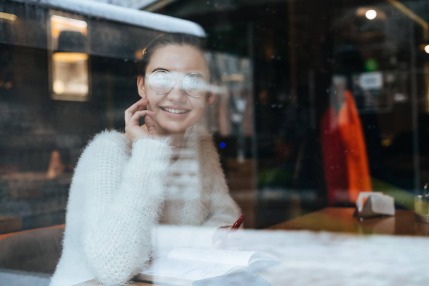 schöne junge Freiberuflerin sitzt im Café, trägt eine Brille, telefoniert und lächelt - Foto, Bild