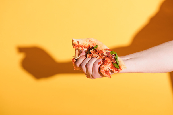 partial view of woman squeezing piece of pizza in hand on yellow background - Foto, Imagem