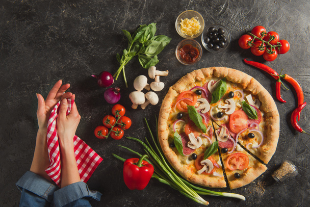 cropped shot of female hands and cooked italian pizza with fresh ingredients on dark tabletop - Photo, Image